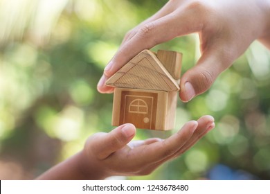  hand is giving a model of a house to child's hand, Concept for Investing in long-term real estate for the future. - Shutterstock ID 1243678480
