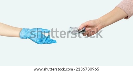 Hand giving money US dollars another hand in blue medical glove on grey background. Paid medicine. Costs for the medical insurance