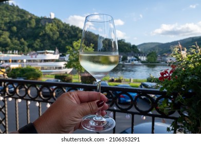 Hand with glass of white quality riesling wine served on outdoor terrace in Mosel wine region with Mosel river and old German town on background in sunny day, Germany