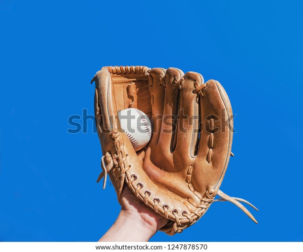 Hand in glove for a baseball game caught a\
leather white ball on a blue sky background. Sports contests.\
Victory. Achievement of\
success.