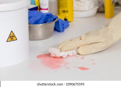 hand with glove cleaning a pink liquid, in the corner of the image a boat labeled as biological risk