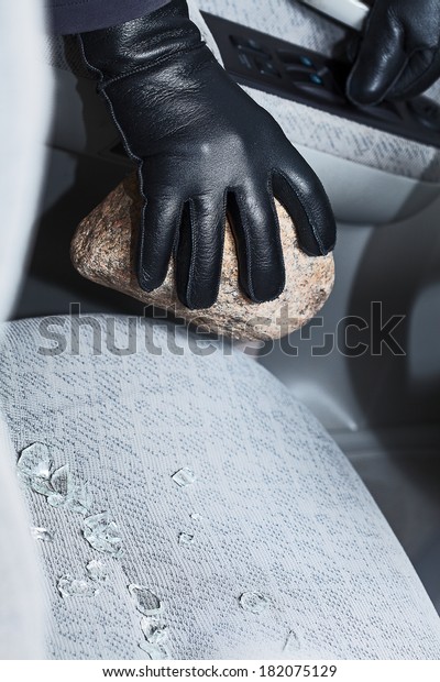 A hand in a glove holding a stone after breaking into\
a car