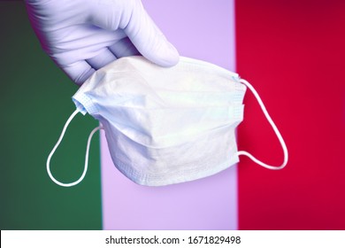 A hand glove holds a mask against the background of the Italian flag. The fight against coronavirus in Italia