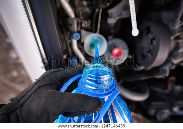 Hand in gloves holding bottle with non-freezing\
washer fluid and pouring it into windshield washer tank in winter.\
Replacement technical fluids according to season. Washer reservoir\
completely filled