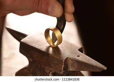 hand of a goldsmith punches a hallmark into a golden ring on an anvil, close up with copy space,  focus, narrow depth of field