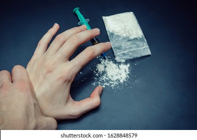 Hand Grabs The Hand Of A Drug Addict With A Package Of Drugs, A Syringe On A Black Background Close-up. You Can Stop Drug Addiction By Rehabilitation In A Rehabilitation Center.