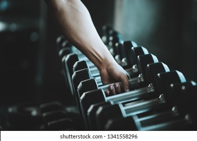 Hand Grasp Dumb Bell From Rack Of Fitness Shop In Cool Tone