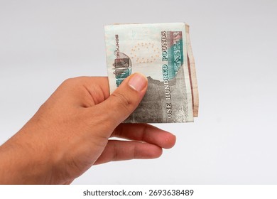 Hand grasping a small stack of Egyptian Pound banknotes (100 EGP notes) isolated on a white background. Represents payment, cash, or giving money