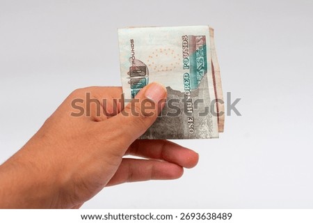 Hand grasping a small stack of Egyptian Pound banknotes (100 EGP notes) isolated on a white background. Represents payment, cash, or giving money