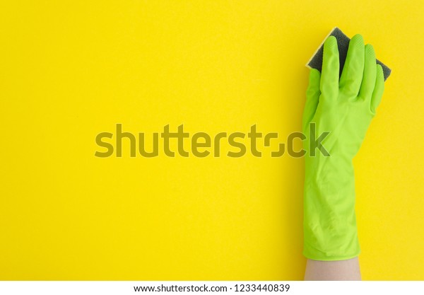 Hand in green glove with sponge on yellow\
background. Flat lay copy\
space