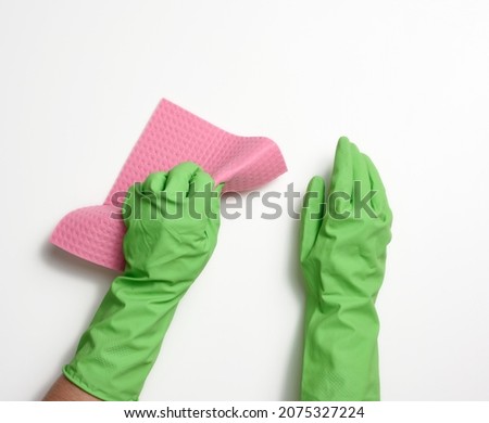 hand in a green rubber glove holds a soft sponge for cleaning surfaces on a white background