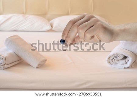 Hand gripping small security camera, portability and convenience, discreet monitoring, video surveillance inviting bedroom with fresh linens and neatly folded towels on bed, Hotel room interior