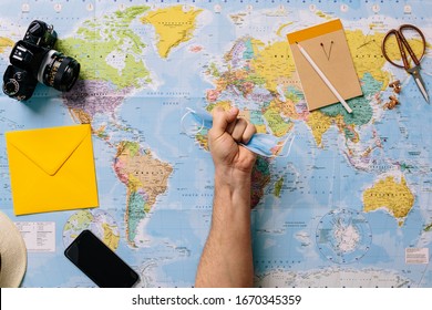 A Hand Grips A Clinical Mask Tightly And Furiously With A World Map In The Background. Vacation Travel Cancellation Concept Due To Covid-19 Coronavirus