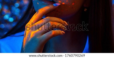 Hand and hair of a girl model painted with neon colored paints in the light of ultraviolet lamps.