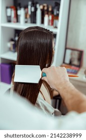 Hand Of Hairdresser Brushing Long And Shiny Dark Hair Of Young Woman At Beauty Salon. Hair Care