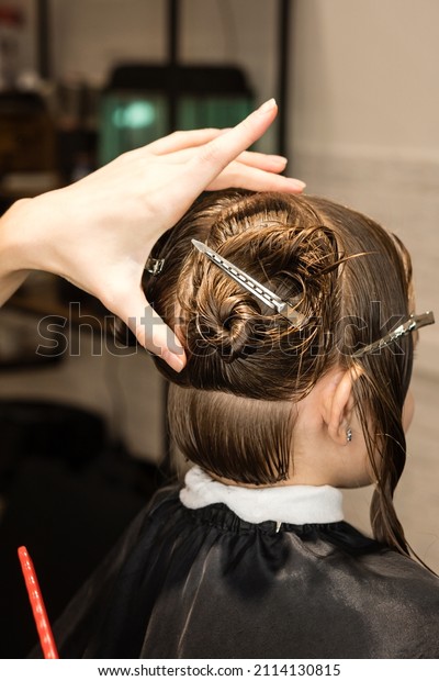 Hand\
of hairdresser doing haircut of kid with hair clips on her hair in\
salon. Hairtician cuts wet hair of child combing with comb. Little\
Girl Client with Short Bob Hair. Close Up Back\
View
