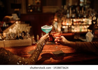 Hand of a happy loving couple with cocktail glasses, celebrating valentines day at the bar. Selective focus on drinks in hands of young couple - Powered by Shutterstock