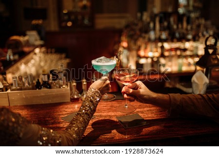 Hand of a happy loving couple with cocktail glasses, celebrating valentines day at the bar. Selective focus on drinks in hands of young couple
