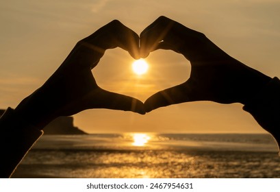 Hand heart shape silhouette made on a beach against the sun and sky of a sunrise or sunset