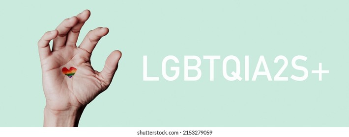 hand of with a heart-shaped rainbow flag and text LGBTQIA2S+ standing for lesbian, gay, bisexual, transgender, queer, intersex, asexual, two spirit and more, in a panoramic format to use as web banner
