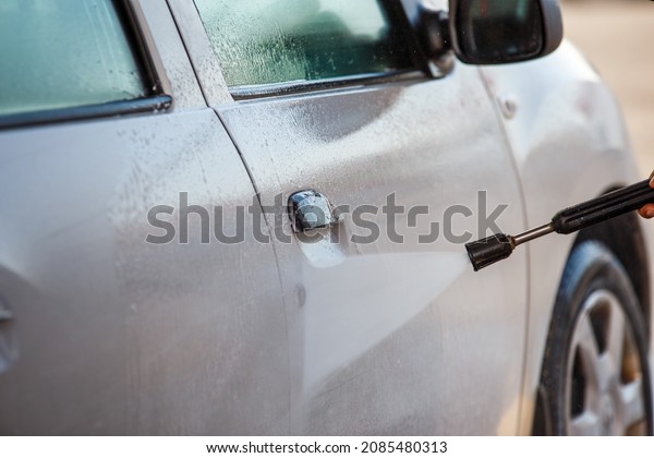 hand\
with high pressure washer washing white car at public self-service\
car washing station, close-up with selective\
focus