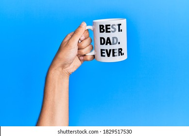 Hand Of Hispanic Man Holding Best Dad Ever Coffee Cup Over Isolated Blue Background.