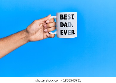 Hand Of Hispanic Man Holding Best Dad Ever Coffee Cup Over Isolated Blue Background.