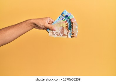 Hand of hispanic man holding canadian dollars over isolated yellow background.
