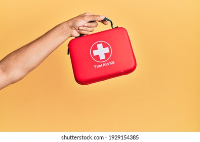 Hand of hispanic man holding first aid kit over isolated yellow background.