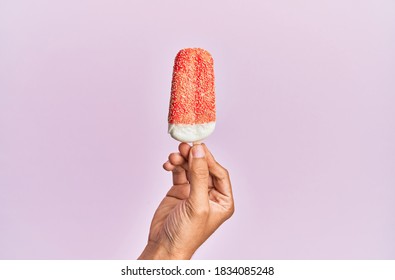 Hand Of Hispanic Man Holding Ice Cream Over Isolated Pink Background.