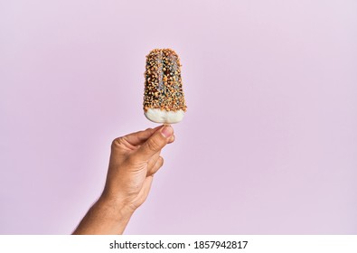 Hand Of Hispanic Man Holding Ice Cream Over Isolated Pink Background.