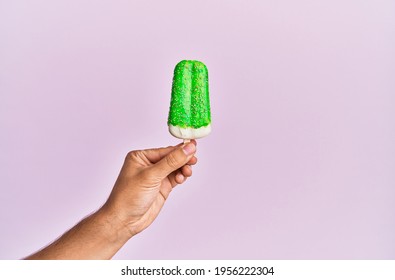 Hand Of Hispanic Man Holding Ice Cream Over Isolated Pink Background.