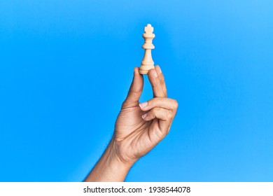 Hand of hispanic man holding king chess piece over isolated blue background.