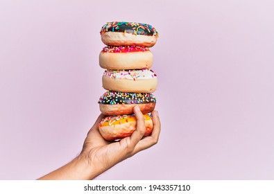 Hand of hispanic man holding tower of donuts over isolated pink background. - Powered by Shutterstock