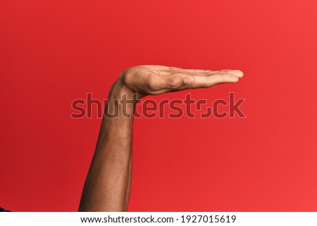Hand of hispanic man over red isolated background with flat palm presenting product, offer and giving gesture, blank copy space 