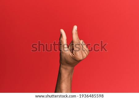 Hand of hispanic man over red isolated background picking and taking invisible thing, holding object with fingers showing space 