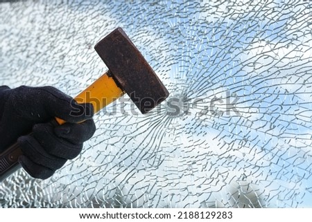 Man’s hand is hitting a window from safety glass with a heavy hammer, vandalism and burglary concept, copy space, selected focus
