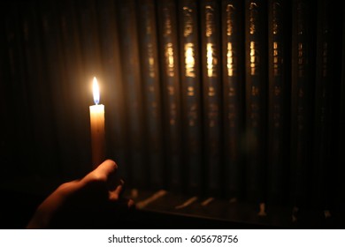 a hand hold a candle and lights up the bookcase.
  Orthodox religious Jew during the traditional Bedikas Chometz prior to the onset of Passover.