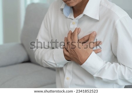 hand hold chest with heart attack symptoms, asian man working hard have chest pain caused by heart disease, leak, dilatation, enlarged coronary heart, press on the chest with a painful expression
