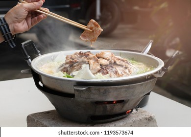 Hand hold chopsticks with pork dishes grill korean barbecue with pork,shrimp,beef,chicken, vegetable and soup on hot pan. or Thai style thai barbecue buffet with the sunlight in Thailand.Moo Kratha
