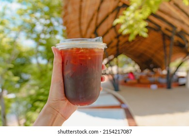 Hand hold a glass of iced americano black coffee without sugar in summer with blue sky background. Stop using Plastic straws ready to drink.