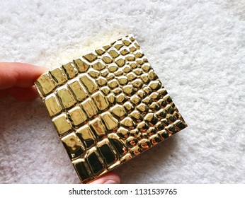 Hand Hold Gold Shinny Plastic Snake Skin Pattern Material Cosmetics Box On White Fluffy Fabric Backgrounds