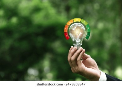 Hand hold light bulb with energy efficient rating. Energy saving rate for reduce carbon footprint.Save cost green energy. Net zero. Renewable energy sources. Green House. - Powered by Shutterstock