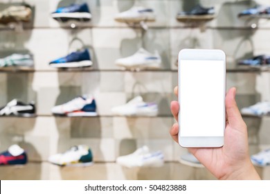 Hand Hold Mobile Phone With Sport Shoes On Shelves In The Store Blur For Background