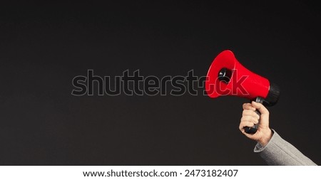 Hand is hold red megaphone and wear grey suit on black background.	

