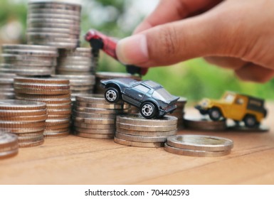 Hand Hold Red Toy Car On Pile Rolls Ladder Of Coins Led To Top And Miniature Cars On Money, Wood Table Green Natural Bright Light Bokeh Background