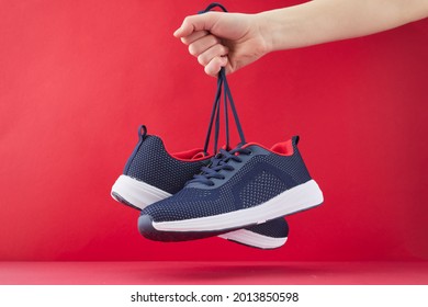 Hand hold sports shoes on red background. Holding new fashion sneakers for running. Choosing and buy of new sneakers. - Powered by Shutterstock