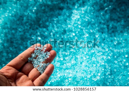 A hand hold or touching plastic pellets , plastic polymer dye granules color clear blue
