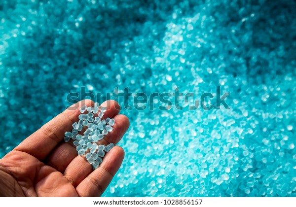 A hand hold or touching plastic\
pellets , plastic polymer dye granules color clear\
blue