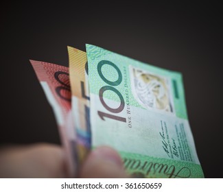 A Hand Holding A 20,50 And 100 Australian Dollar Notes On A Black Background